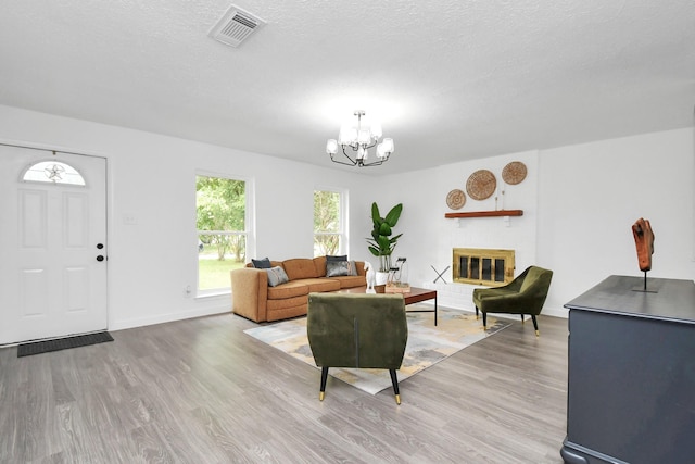 living room with a fireplace, light hardwood / wood-style floors, a textured ceiling, and an inviting chandelier