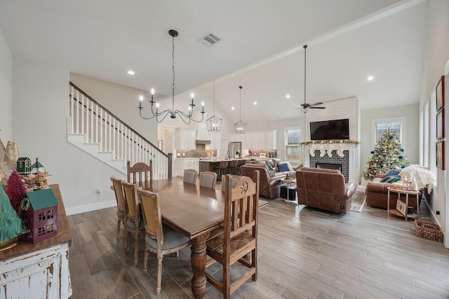 dining area with lofted ceiling, wood-type flooring, ceiling fan with notable chandelier, and a brick fireplace