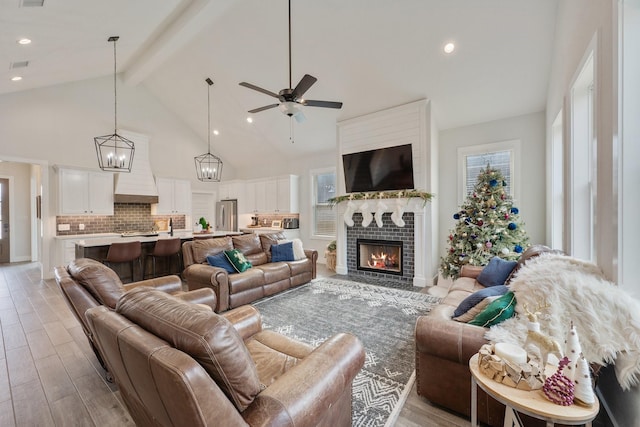 living room with beam ceiling, a fireplace, ceiling fan, and light hardwood / wood-style flooring