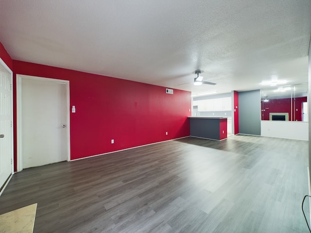 unfurnished living room featuring a textured ceiling, ceiling fan, and dark wood-type flooring