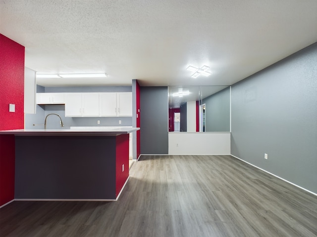 kitchen with a textured ceiling, hardwood / wood-style flooring, white cabinetry, and sink