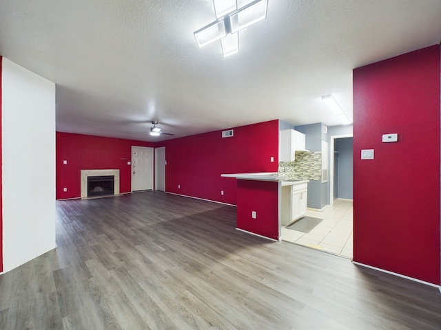 unfurnished living room with ceiling fan, light hardwood / wood-style floors, and a textured ceiling