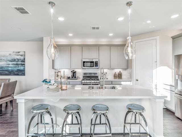 kitchen with gray cabinets, hardwood / wood-style floors, hanging light fixtures, and appliances with stainless steel finishes