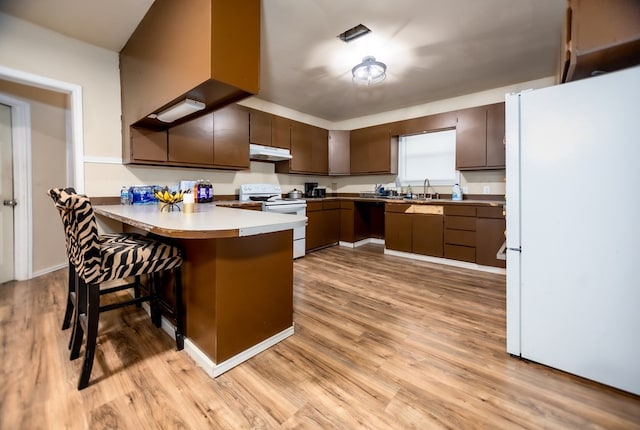 kitchen with kitchen peninsula, a kitchen bar, white appliances, sink, and light hardwood / wood-style floors