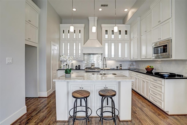 kitchen with sink, stainless steel microwave, white cabinetry, and a kitchen island with sink