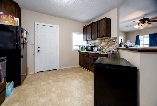 kitchen with black fridge, ceiling fan, a textured ceiling, tasteful backsplash, and dark brown cabinets