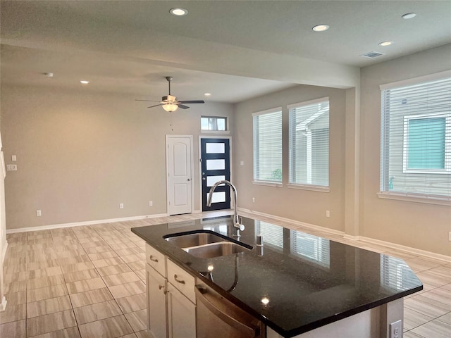 kitchen featuring sink, white cabinets, a center island with sink, stainless steel dishwasher, and dark stone counters