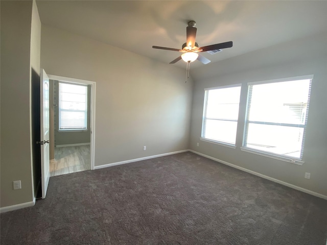 spare room with dark colored carpet, lofted ceiling, a healthy amount of sunlight, and ceiling fan