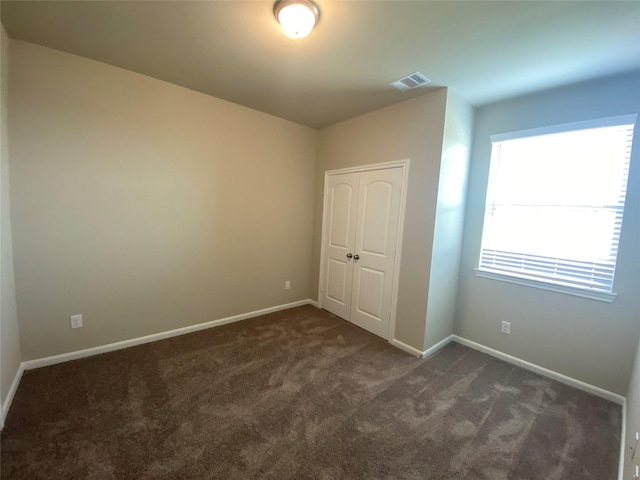 unfurnished bedroom with dark carpet and a closet