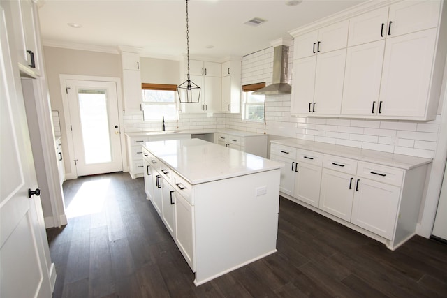 kitchen with wall chimney exhaust hood, dark wood-type flooring, a kitchen island, decorative light fixtures, and white cabinets