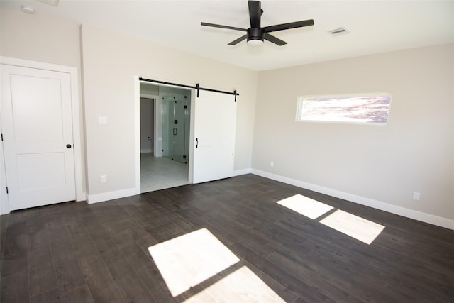 unfurnished bedroom with a barn door, ceiling fan, and dark hardwood / wood-style floors