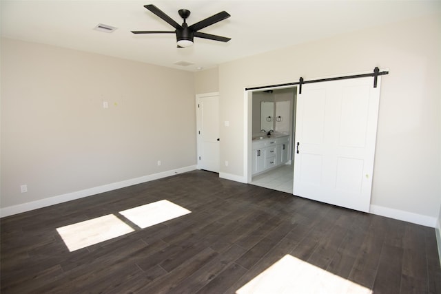 unfurnished bedroom featuring sink, dark hardwood / wood-style floors, a barn door, ceiling fan, and connected bathroom