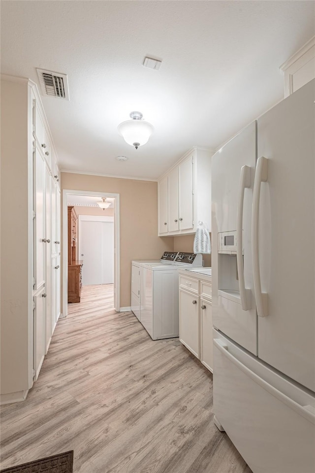 laundry room with washing machine and dryer, light hardwood / wood-style flooring, and cabinets