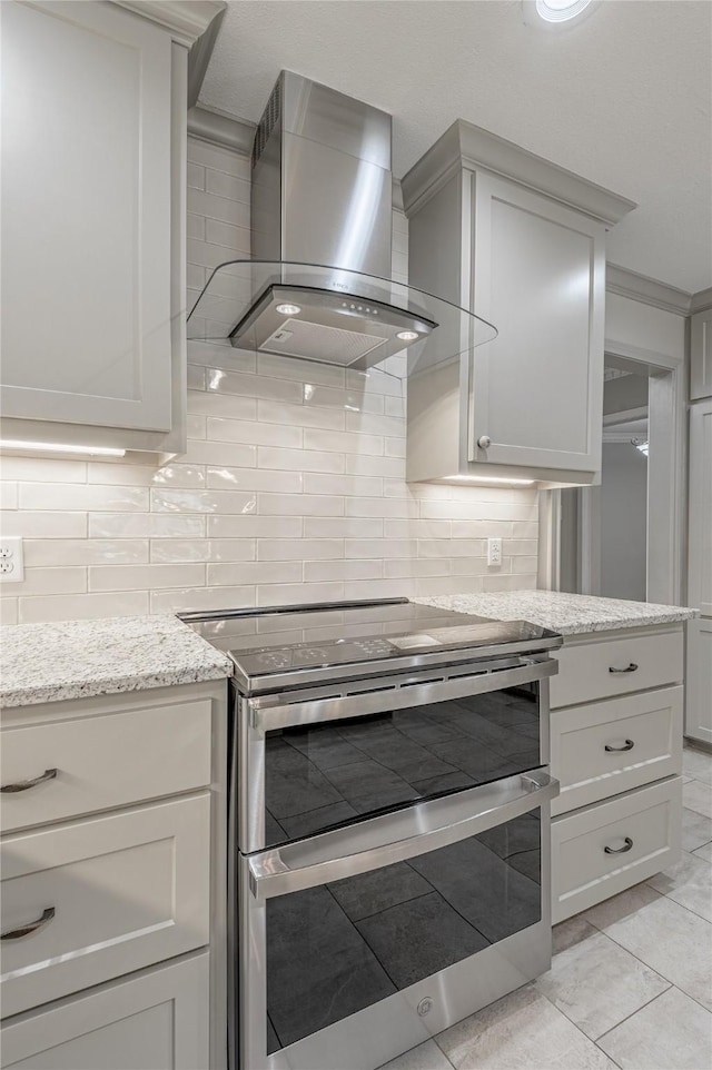 kitchen featuring backsplash, range with two ovens, wall chimney exhaust hood, and light stone counters