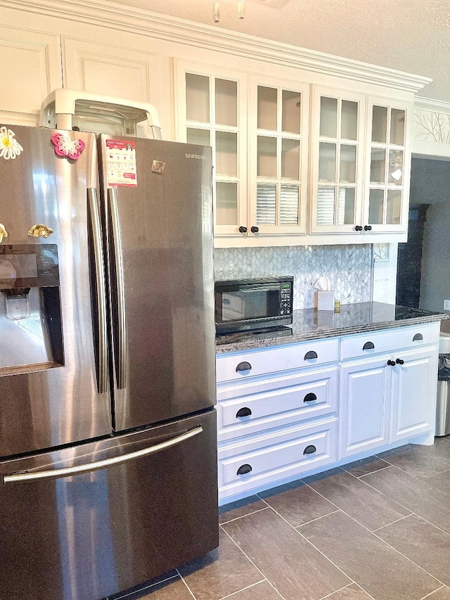 kitchen with stainless steel fridge, ornamental molding, dark stone counters, dark tile patterned floors, and white cabinetry