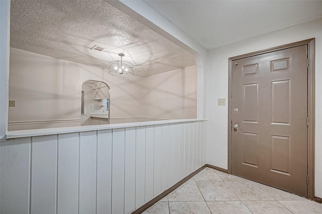 entryway featuring light tile patterned flooring, a textured ceiling, and a chandelier