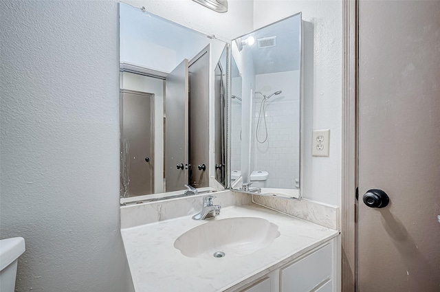 bathroom with tiled shower, vanity, and toilet