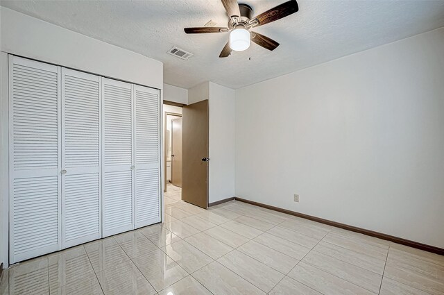 unfurnished bedroom featuring ceiling fan, light tile patterned floors, a textured ceiling, and a closet