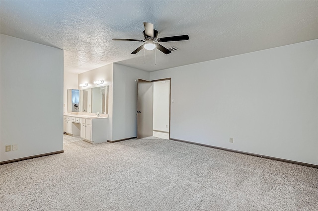 unfurnished bedroom featuring ceiling fan, sink, ensuite bathroom, light colored carpet, and a textured ceiling