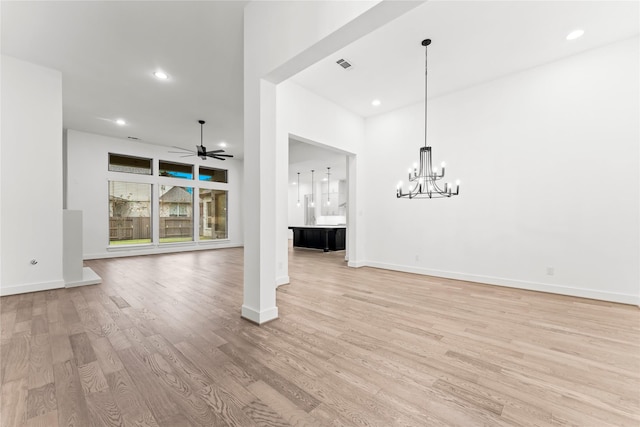 unfurnished living room with ceiling fan with notable chandelier and light hardwood / wood-style floors