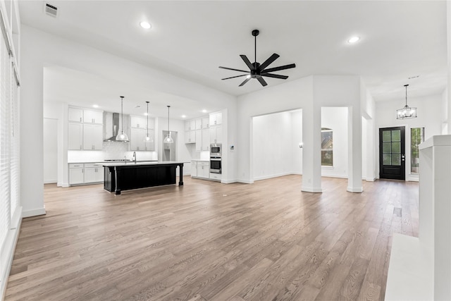 unfurnished living room featuring sink, ceiling fan with notable chandelier, and light wood-type flooring