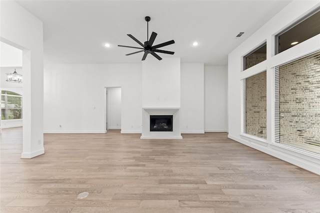 unfurnished living room with plenty of natural light, light hardwood / wood-style floors, and ceiling fan with notable chandelier