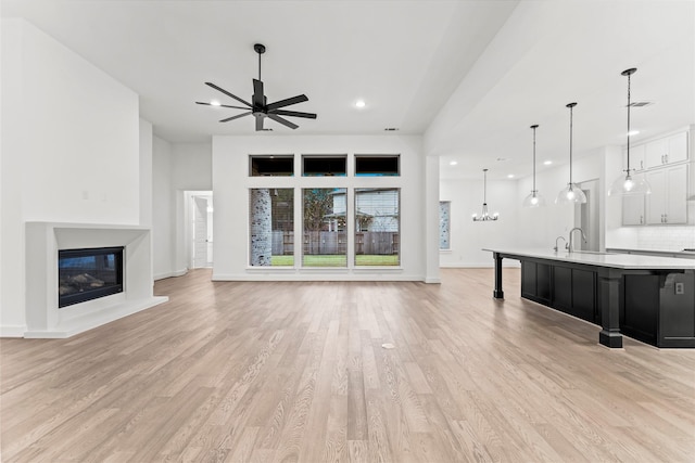 unfurnished living room with light wood-type flooring, ceiling fan, and sink