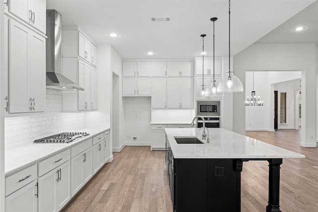 kitchen featuring pendant lighting, a kitchen island with sink, sink, wall chimney exhaust hood, and appliances with stainless steel finishes