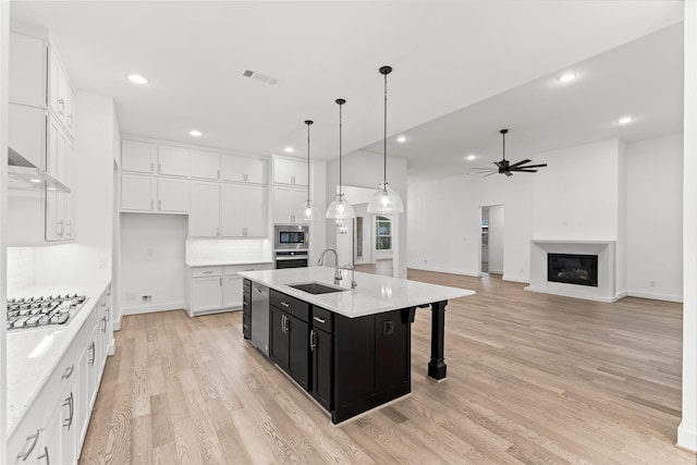 kitchen featuring appliances with stainless steel finishes, a kitchen island with sink, sink, decorative light fixtures, and white cabinets