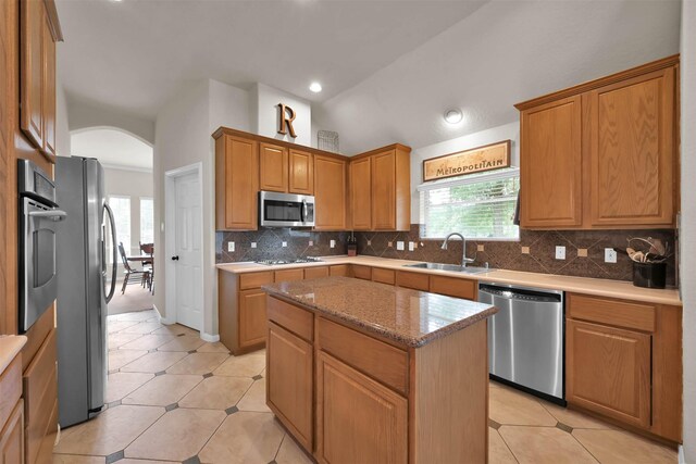 kitchen featuring appliances with stainless steel finishes, tasteful backsplash, vaulted ceiling, sink, and a kitchen island