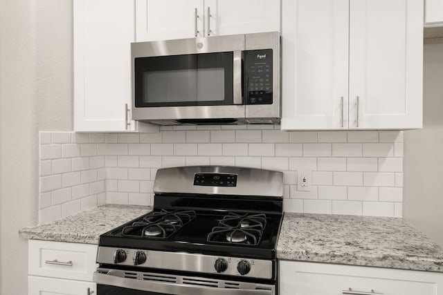 kitchen featuring white cabinets, light stone countertops, stainless steel appliances, and tasteful backsplash