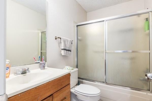 full bathroom with combined bath / shower with glass door, vanity, a textured ceiling, and toilet