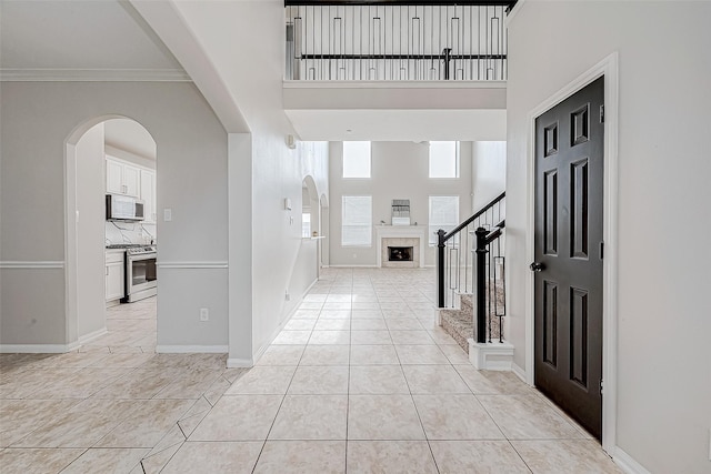 entryway featuring a tile fireplace, a towering ceiling, light tile patterned floors, and ornamental molding