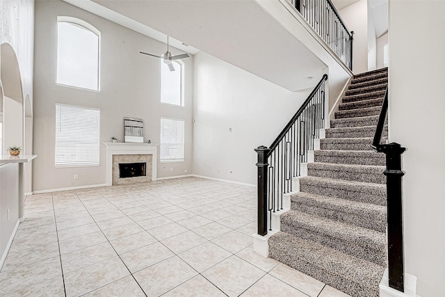 unfurnished living room with ceiling fan, a tile fireplace, light tile patterned floors, and a high ceiling