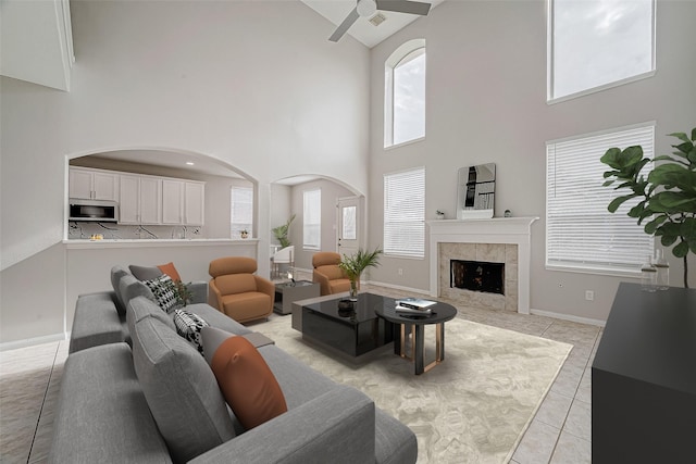 living room with ceiling fan, a towering ceiling, a fireplace, and light tile patterned floors