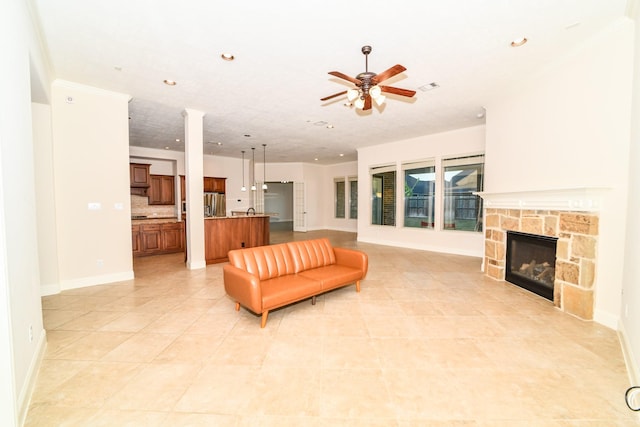 tiled living room with ceiling fan, a stone fireplace, and ornamental molding