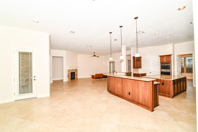 kitchen featuring double oven, ceiling fan, a fireplace, hanging light fixtures, and a large island