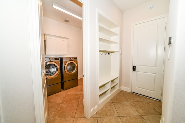 clothes washing area featuring washer and clothes dryer, light tile patterned floors, and cabinets