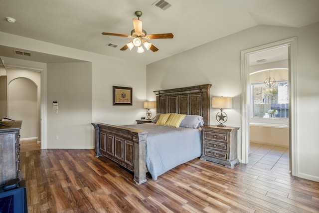 bedroom with vaulted ceiling, ensuite bath, wood-type flooring, and ceiling fan with notable chandelier