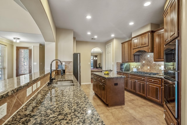 kitchen with decorative backsplash, stainless steel appliances, sink, dark stone countertops, and a center island