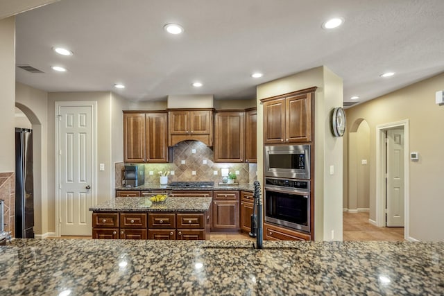 kitchen with backsplash, stainless steel appliances, and dark stone counters