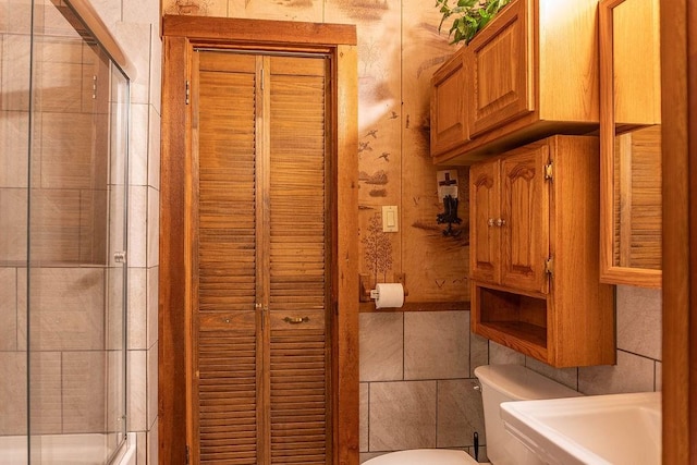 bathroom featuring toilet, tile walls, and a shower with shower door