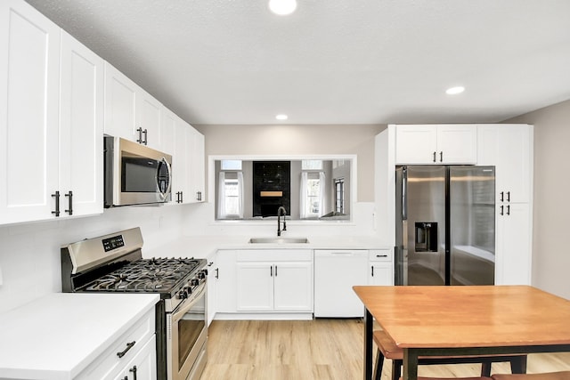 kitchen with sink, white cabinets, light hardwood / wood-style floors, and appliances with stainless steel finishes