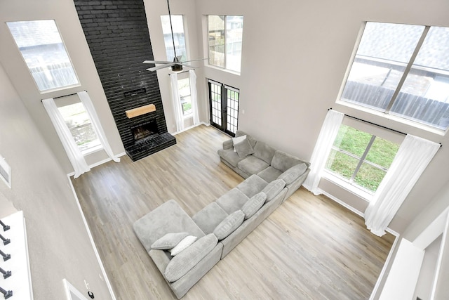 living room with ceiling fan, light hardwood / wood-style floors, a high ceiling, and a brick fireplace