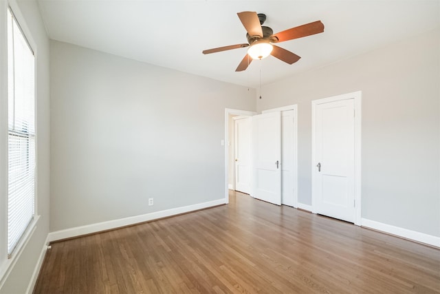 unfurnished bedroom featuring ceiling fan, wood-type flooring, and two closets