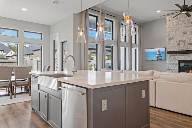 kitchen featuring gray cabinetry, dishwasher, a fireplace, and hanging light fixtures