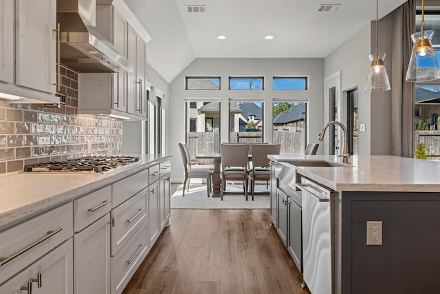 kitchen featuring a kitchen island with sink, wall chimney range hood, hanging light fixtures, hardwood / wood-style flooring, and appliances with stainless steel finishes