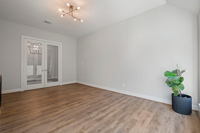 empty room with hardwood / wood-style floors, vaulted ceiling, french doors, and a notable chandelier