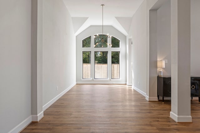 unfurnished living room featuring hardwood / wood-style floors, vaulted ceiling, and a notable chandelier