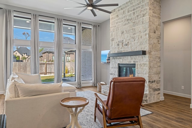 living area featuring a stone fireplace, ceiling fan, and hardwood / wood-style flooring